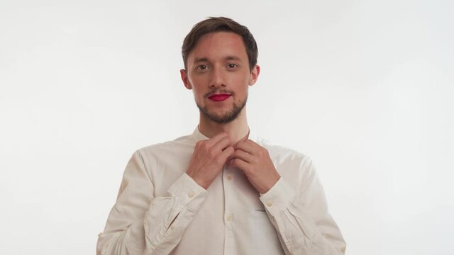 European single smiling happy person wear business shirt, use make-up &ndash; red lipstick on lips. Prety man unbuttons clothing, undressing like a stripper, stare at camera isolated on white background.