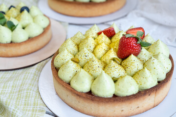 Three round shortbread pie with green pistachio cream and strawberry jam by the window. Pistachio pie with cream cheese