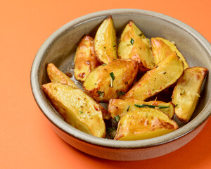 Baked potato with rosemary served in a ceramic bowl over orange background. Delicious idea for dinner.