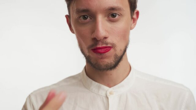 One confident effeminate European handsome bearded man with makeup &ndash; red lipstick on lips wear shirt, look at camera, eat with pleasure sweet candy isolated on white background close up. Male portrait
