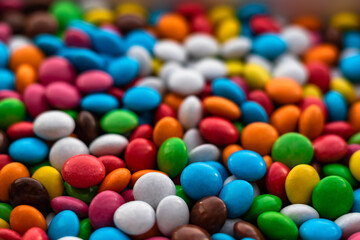 Lots of multicolored round dragee candies fill the entire frame. Focus on the foreground. The background fades into bokeh. Background from multicolored food.