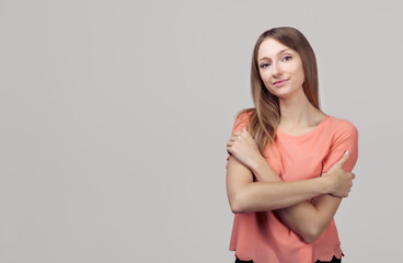 Portrait of gentle lovely beautiful young woman with blonde straight hair hugging herself, expresses self love and care