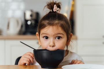 toddler girl picky eater at home kitchen. learning o eat with spoon. bad table manners of kid