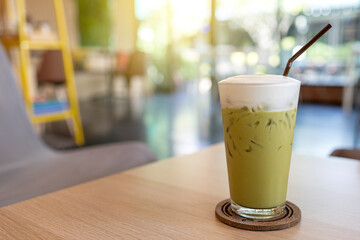 Iced green tea glass on wooden table on blurred coffee shop background.