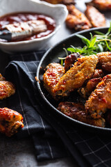 Chicken wings barbeque in a cast iron baking dish with BBQ sauce and rosemary
