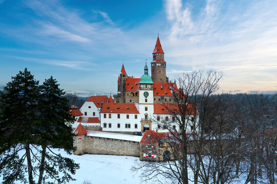 Castle in winter. Romantic fairytale castle in picturesque highland landscape, covered in snow. Castle with white church, high towers, red roofs, stone walls. Bouzov castle, Czech republic.