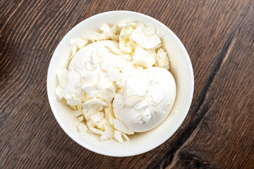 Two whole white chicken eggs are covered with shells. Bowl with eggs and shells. Close up.