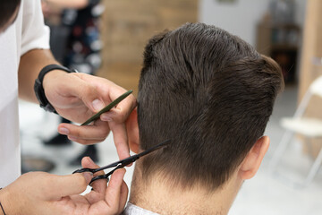 Hairdresser male hands during cutting hair with comb and scissors