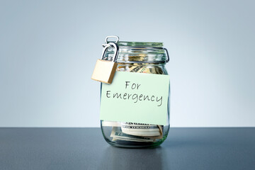 For Emergency savings written on the jar with dollars banknotes money. Concept of money saving for...