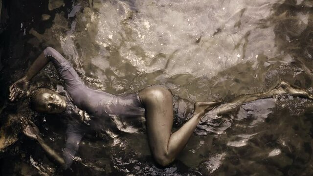graceful woman in water with golden pigment, skin is covered by gold dye, slow motion