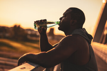 Portrait of young african-american man in sports clothing who is drinking water after exercise. He...