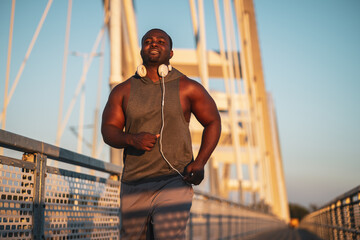 Young happy african-american man is jogging on the bridge in the city.  He is exercising to reduce his body weight. 
