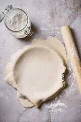 Overhead shot showing process of preparing a pie or fruit tart over a natural stone background. The photo includes flour, pieces of dough and a rolling pin.