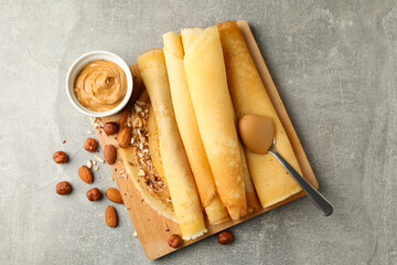 Concept of delicious breakfast with crepes with peanut butter and nuts on gray table
