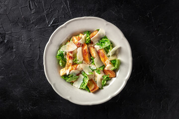 Chicken caesar salad with romaine and Parmesan cheese, top shot on a black background