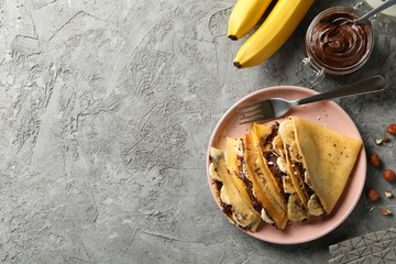Fototapeta na wymiar Concept of delicious breakfast with crepes with chocolate paste, banana and nuts on gray background