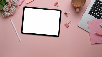 Top view of digital tablet laptop and office supplies on pastel pink background.