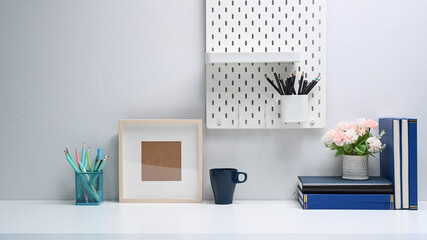 Modern office desk with empty frame, books, stationery and coffee cup on white table.