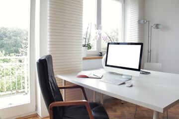 Workspace - the bright home office with the desktop computer with a blank screen on the white wooden table.