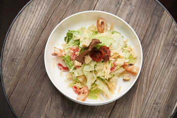 Caesar salad with shrimp on white bowl, on table