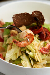 Caesar salad with shrimp on white bowl, on table