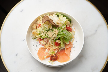 Caesar salad with salmon fish on white bowl