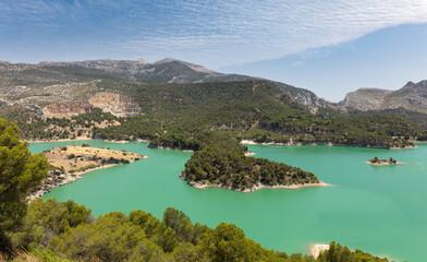The large Guadalhorce reservoir in the mountains of Andalusia in southern Spain in summer. There are several small islands in the lake. It's sunny and there are beautiful clouds in the sky.
