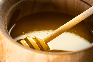 honey in a deep wooden bowl, rustic wooden plate. The wooden spoon drips slowly.