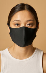 Studio portrait of beautiful young mixed race woman wearing black facial mask, looking at camera while posing isolated over beige background