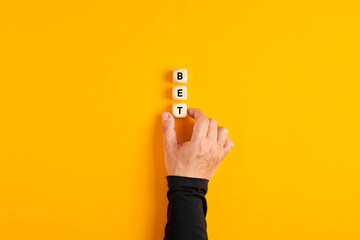 Male hand placing the wooden blocks with the word Bet on yellow background.