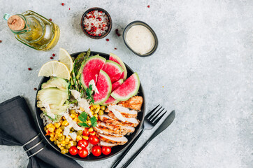 Buddha bowl with brown rice, grilled chicken breast, avocado, tomato, peas, corn, watermelon radish, asparagus with tahini sauce on gray background. Top view