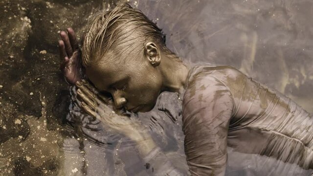 unusual fashion shot with tender woman covered golden paint in water, moving slowly