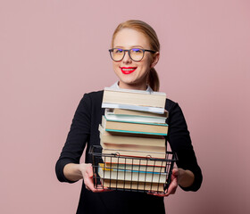 Blonde woman black dress and glasses hold shopping basket with books on pink background