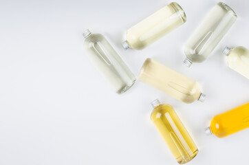 Abstract cosmetic border of lying bottles with different pale colors liquid, silver cap on white background, top view, copy space.