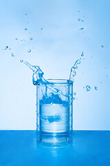 Clear water splashing in a glass on a blue background.