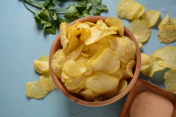 Crispy potato chips in bowl on blue background