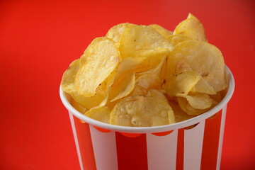 Crispy potato chips in bowl on red background