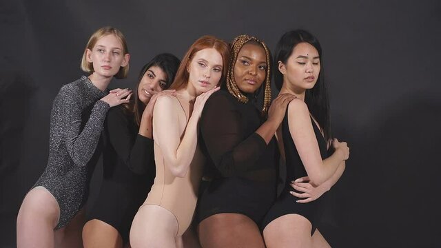 Beautiful multi-ethnic group of models posing at camera, wearing bodysuit, isolated on black background.