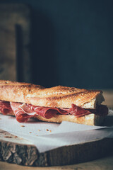 Jamón ibérico in a bread baguette ion a wooden board and in a low key atmosphere.