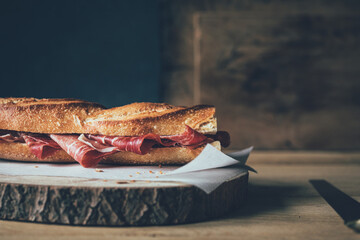 Jamón ibérico in a bread baguette on a wooden board and in a low key atmosphere.