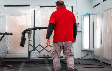 A professional mechanic working in a paint chamber during the coating process of a damaged vehicle. Airbrush technology, high-pressure painting, restyling, automotive wrapping service.