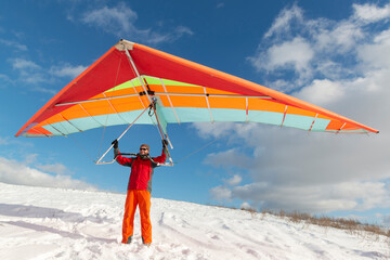 Happy man holding colorful hang glider wing on a slope.
