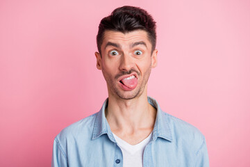 Photo portrait of silly crazy tricky guy showing tongue grimacing isolated pastel pink color background