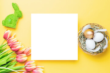 Naklejka na ściany i meble Easter eggs basket. Golden egg in basket with spring tulips, white feathers on pastel yellow background in Happy Easter decoration. Traditional decoration in sun light. Top view.