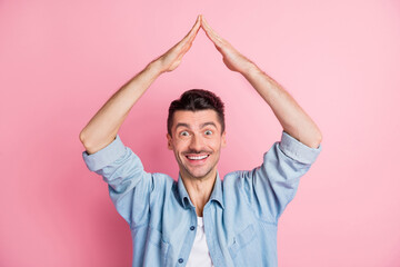 Photo portrait of young man keeping hands over head showing roof insurance safety smiling isolated pastel pink color background