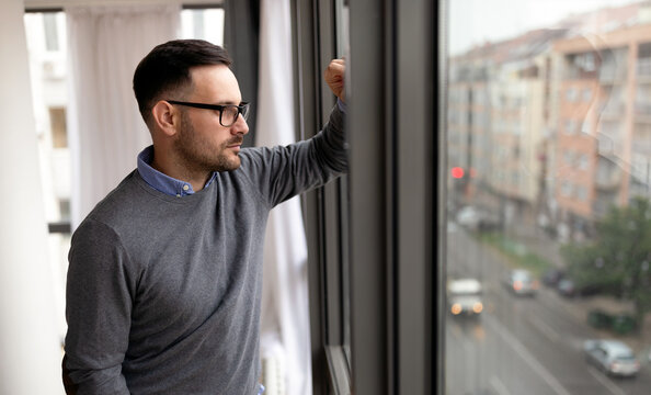 Portrait of man sad and depressed standing at window in despair at home