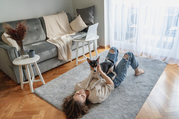 Pretty curly happy young woman smiling while lying at home on carpet with her dog