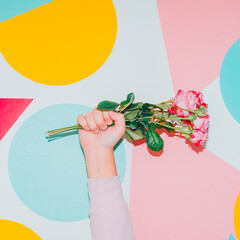 Hand holds spring flower bouquet on colorful background. Modern creative Valentines or woman's day concept. Pop art style