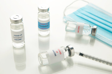 Coronavirus or COVID-19, 2019 - nCoV vaccine in a bottle with syringe and hygiene protective face mask on eflective surface.