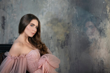 Fototapeta premium Delicate dark-haired woman in a light pink dress with delight on the wall